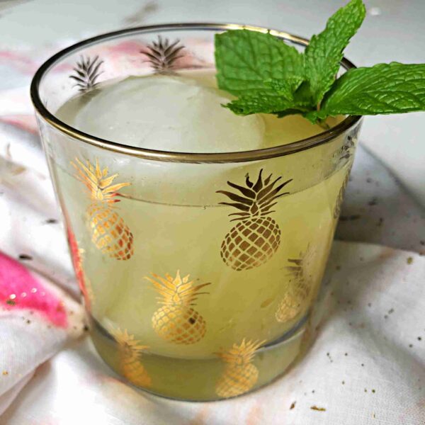A glass covered in gold pineapples full of pineapple ginger mocktail shrub.